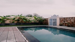 Ein Swimmingpool mit Steinmauer und Holztor, umgeben von Kübelpflanzen und einer Rasenfläche.