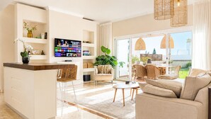 A modern living room with a sofa, a dining area, a kitchen with a TV, and a balcony with plants. - Pueblo Paraiso Apt, 6 pools, gym & spa (Benahavís)