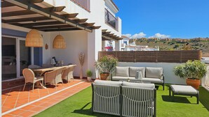 A patio with a dining table, chairs, and a sofa. There is a view of a hillside in the background. - Pueblo Paraiso Apt, 6 pools, gym & spa (Benahavís)