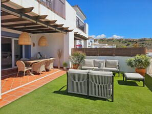 Eine Terrasse mit Esstisch, Stühlen und einer Couch. Im Hintergrund ist ein Hügel zu sehen.