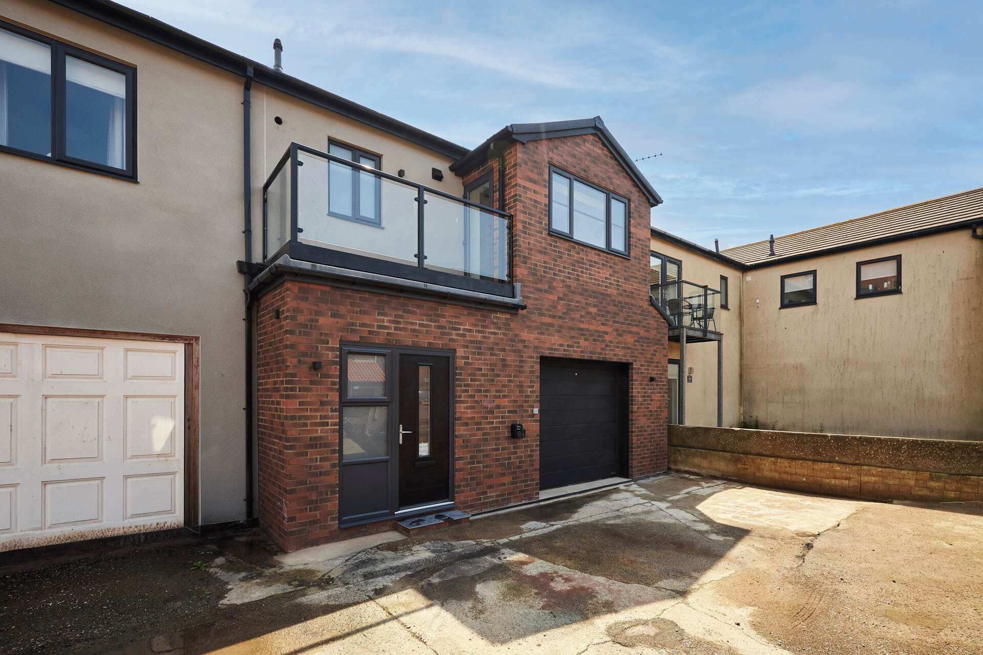 Une maison à deux étages avec un garage, un balcon et une façade en briques.