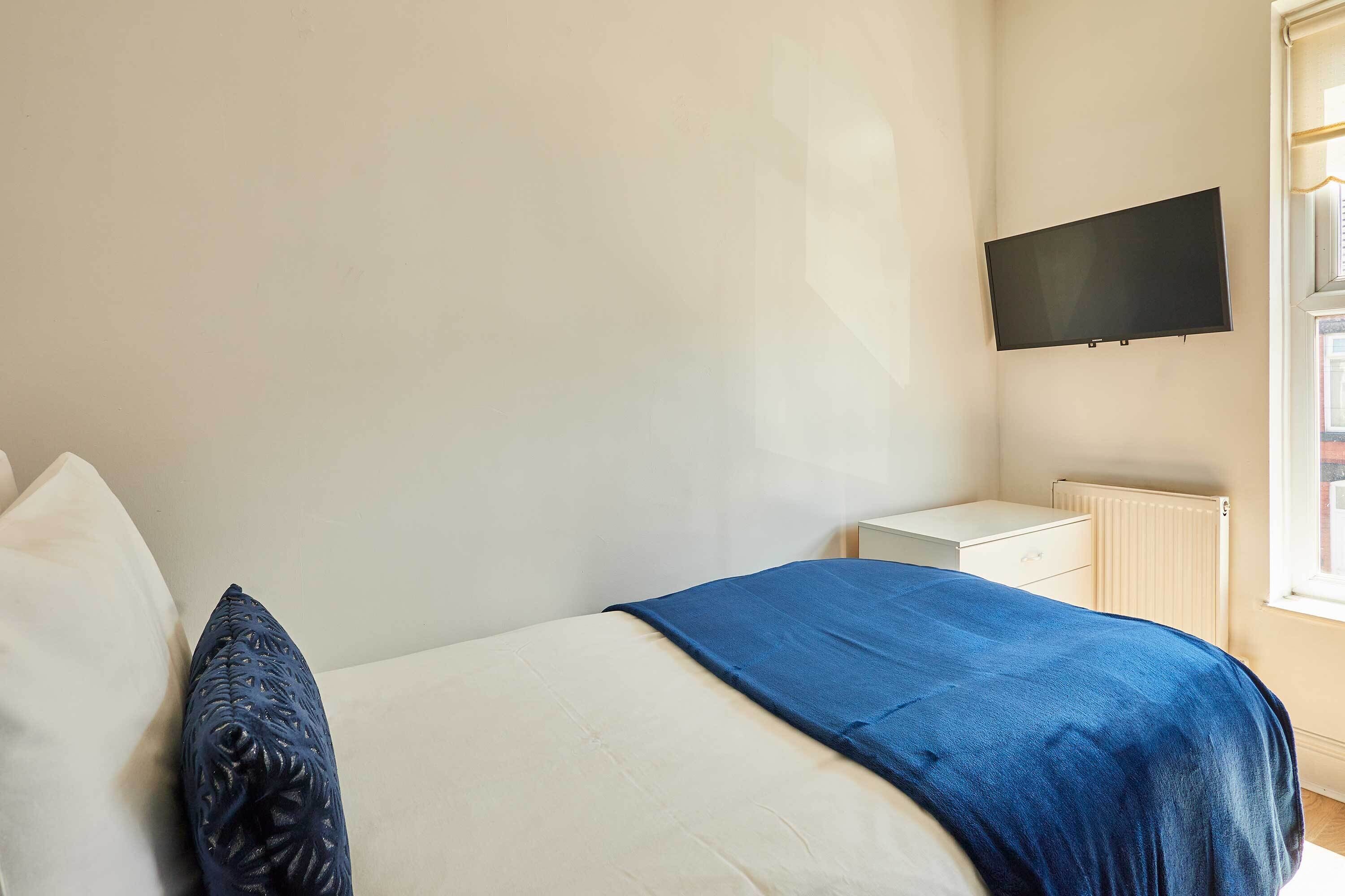 Une chambre à coucher avec un lit, une table de chevet, un téléviseur fixé au mur et une fenêtre.