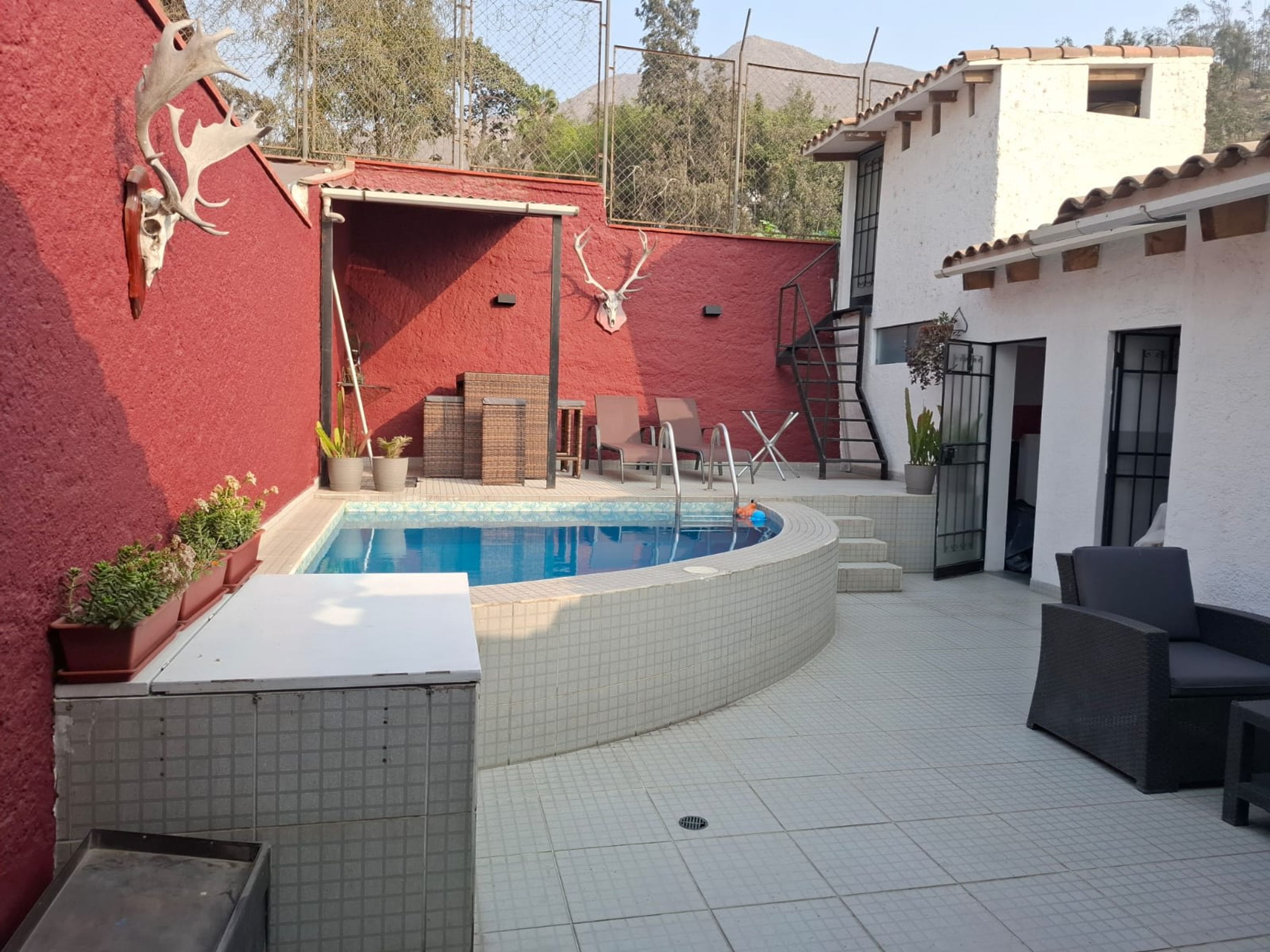 Una piscina con un muro rojo y un edificio blanco al fondo.