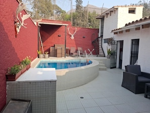 Una piscina con un muro rojo y un edificio blanco al fondo.