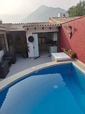 A swimming pool with a tiled deck, a red wall with a mounted animal head, and a view of mountains in the background.