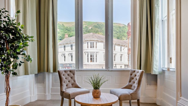 A room with a large window, two upholstered chairs, a round wooden table, and a potted plant. - Host Stay Flat 1 Club Chambers (Malvern)