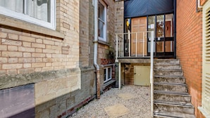 A narrow alleyway with a brick building, a wooden door, and a metal staircase leading to a second-floor entrance. - Host Stay Flat 1 Club Chambers (Malvern)