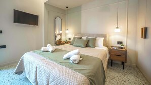 Ein Hotelzimmer mit einem großen Bett, zwei Nachttischen, einem Flachbildfernseher und einem Spiegel.
