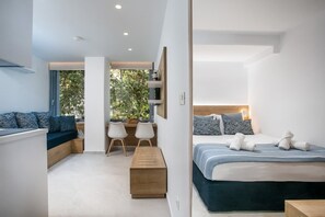 A modern hotel room with a bed, seating area, and a view of greenery outside. - Elegant Blue Rhodes Center Apartment Near the Sea (Rhodes)