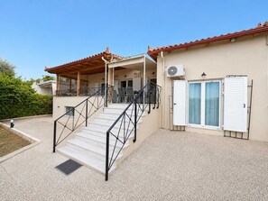 A building with a staircase leading to a covered area, a door with shutters, and a window with a curtain. - Beachside Hideaway - Steps From Lechaio Blue Shore (Corinth)