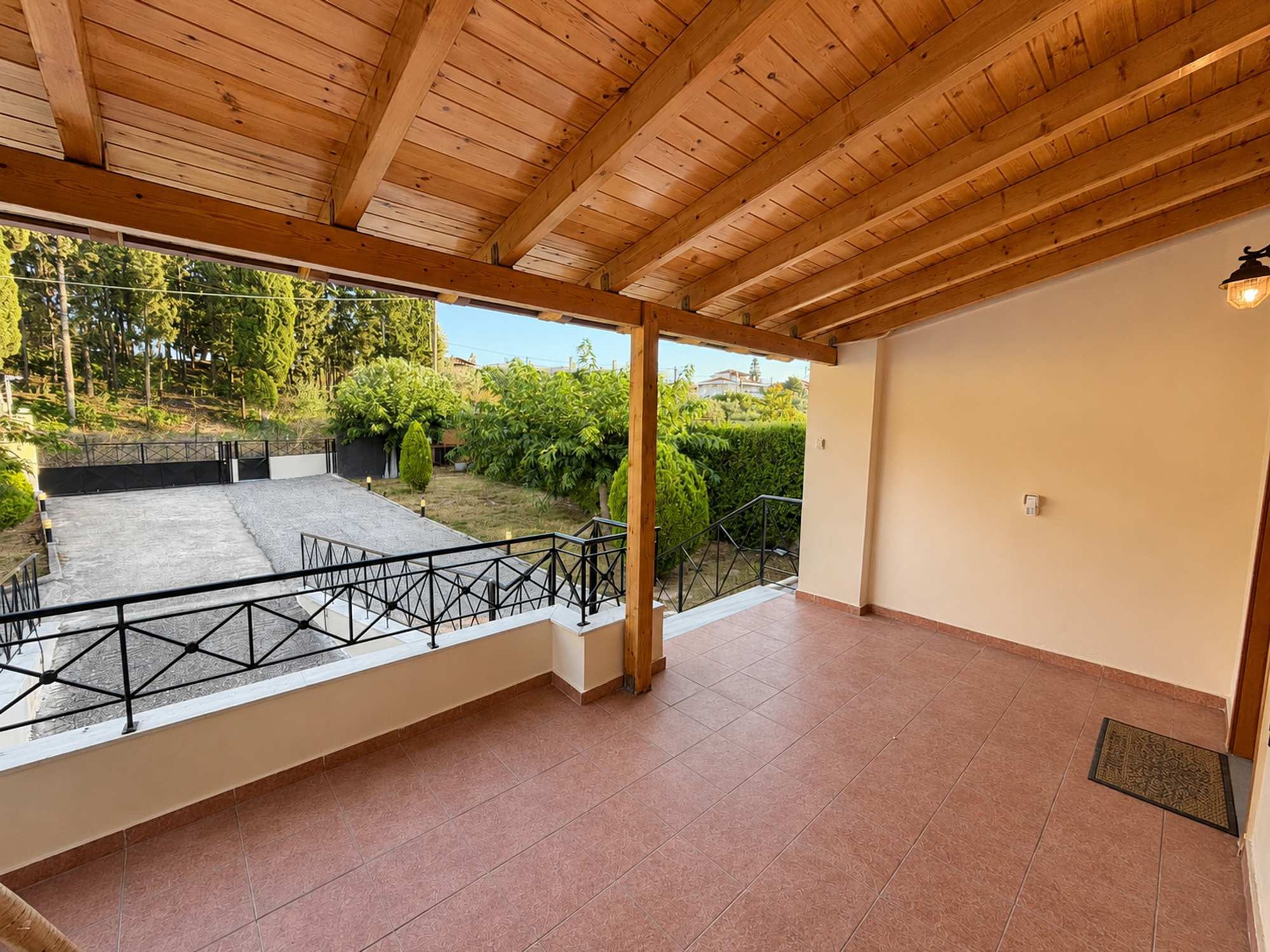 Een ruime kamer met een houten plafond, een balkon met metalen hekwerk en uitzicht op een tuin.