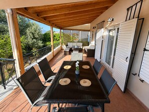 An outdoor patio with a table, chairs, and a view of the surrounding landscape. - Beachside Hideaway - Steps From Lechaio Blue Shore (Corinth)