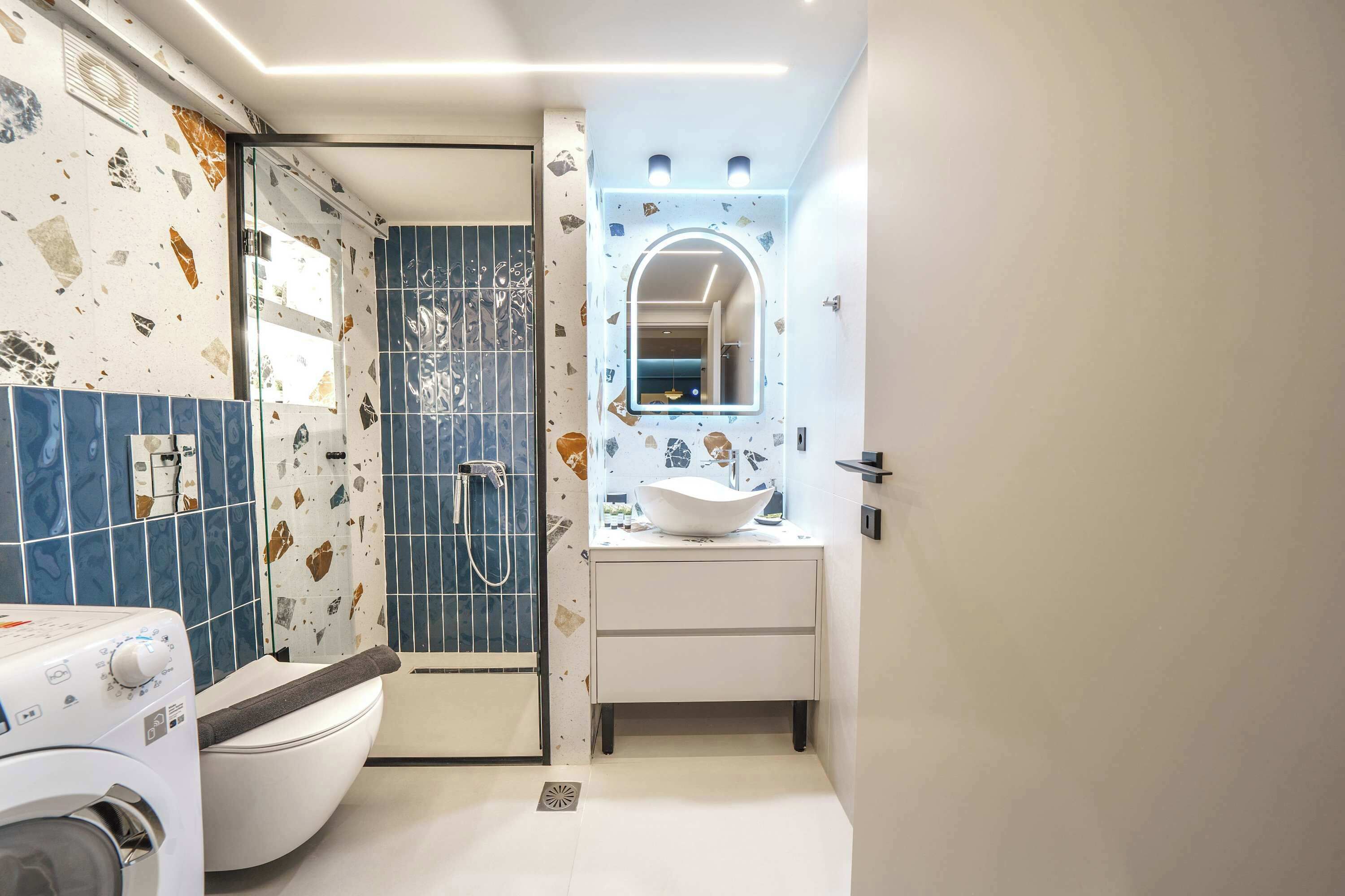 A compact bathroom with a washing machine, a shower, and a sink with a mirror.