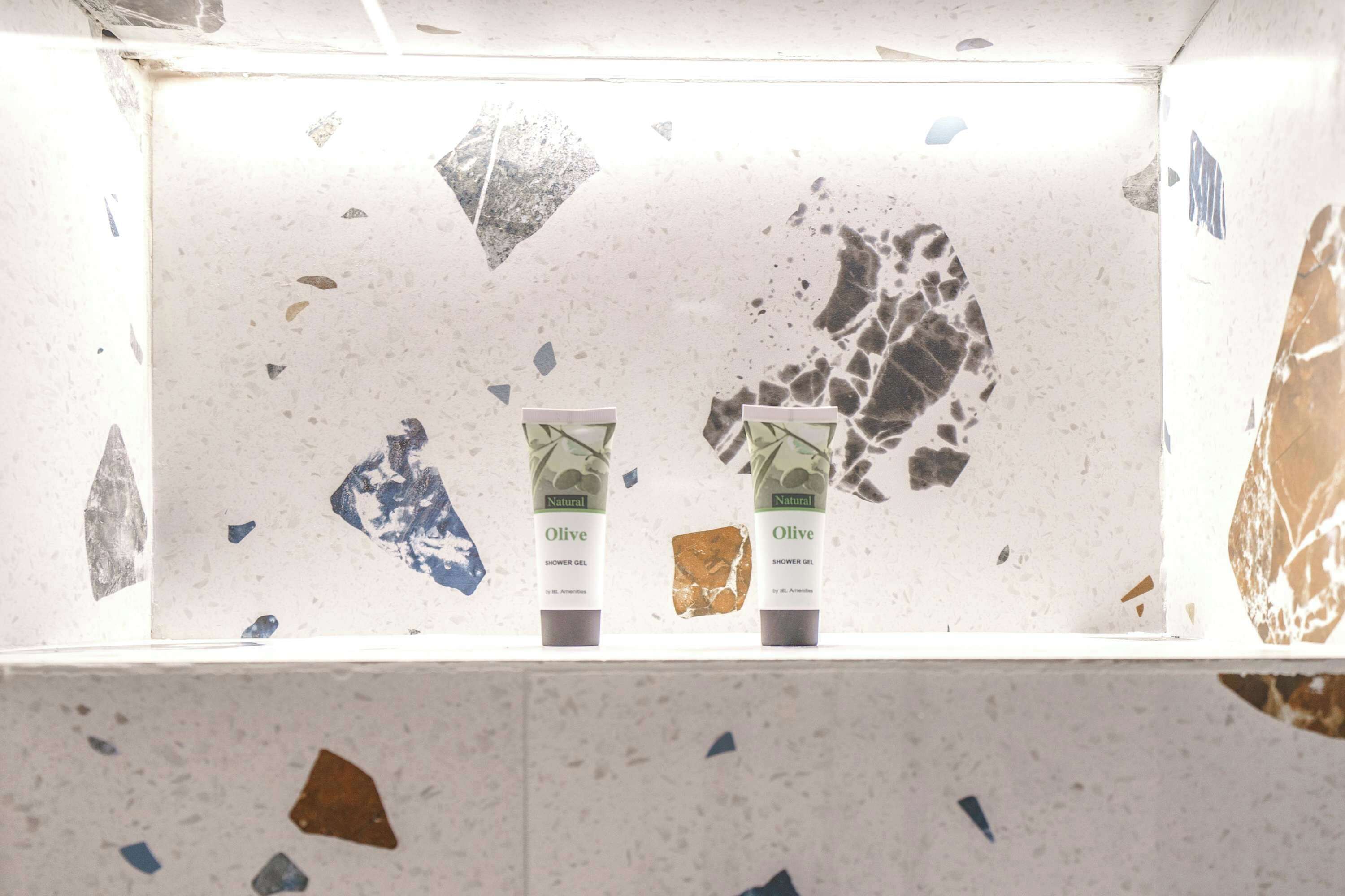 Two shower gel bottles on a shelf with a speckled tile backsplash.