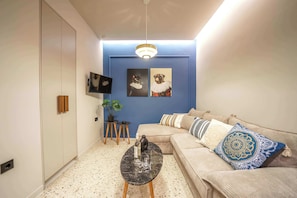 A living room with a sofa, a coffee table, a TV, and artwork on the wall. - Noble Heraklion Suites Crete Azure Suite (Heraklion)