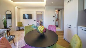 A modern living room with a round table, colorful chairs, a TV, and a kitchen area. - Noble Heraklion Suites Terra Suite in Crete (Heraklion)