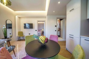 A modern living room with a round table, colorful chairs, a TV, and a kitchen area. - Noble Heraklion Suites Terra Suite in Crete (Heraklion)