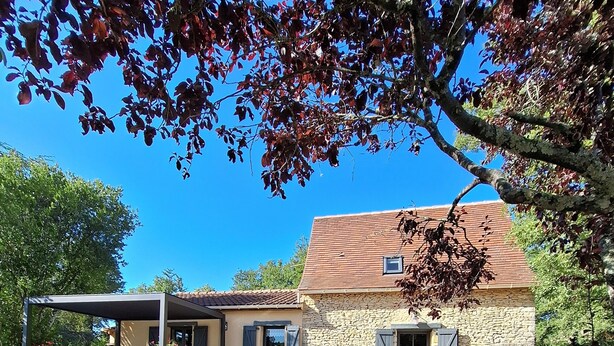 A stone house with a covered patio, a chair, and a clear blue sky.