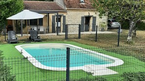 A backyard with a swimming pool, a stone house, and a fenced patio area.