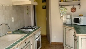 A compact kitchen with a gas stove, sink, and a microwave. There is a small cabinet and a shelf with kitchen items.