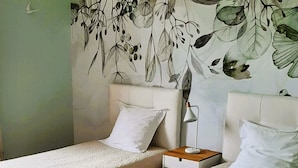 A room with two single beds, a nightstand with a lamp, and a wall with a botanical mural.