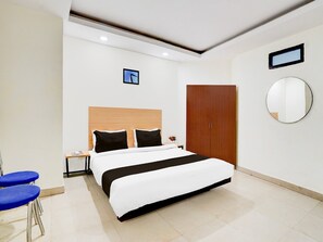 A modern hotel room with a large bed, a wooden wardrobe, a round mirror, and a small table with a chair. - Deluxe Patparganj Near Max Hospital (New Delhi)