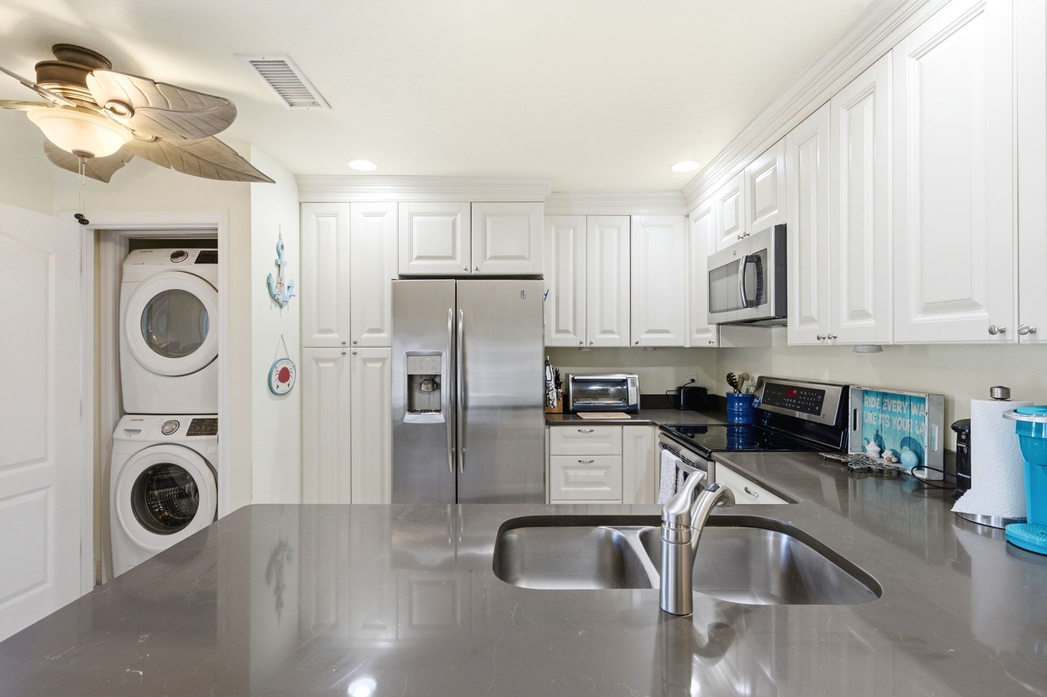 A modern kitchen with stainless steel appliances, white cabinetry, and a built-in washer and dryer.