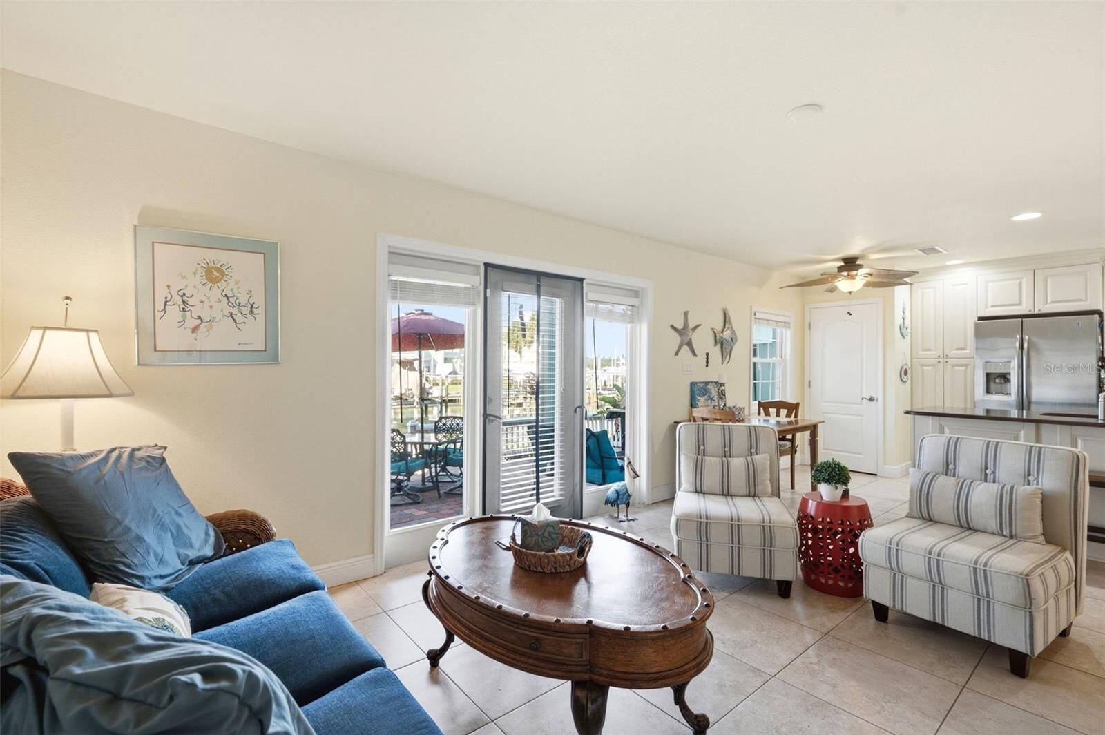 A living room with a sofa, armchairs, a coffee table, and a dining area with a table and chairs. There is a kitchen area with cabinets and a refrigerator.