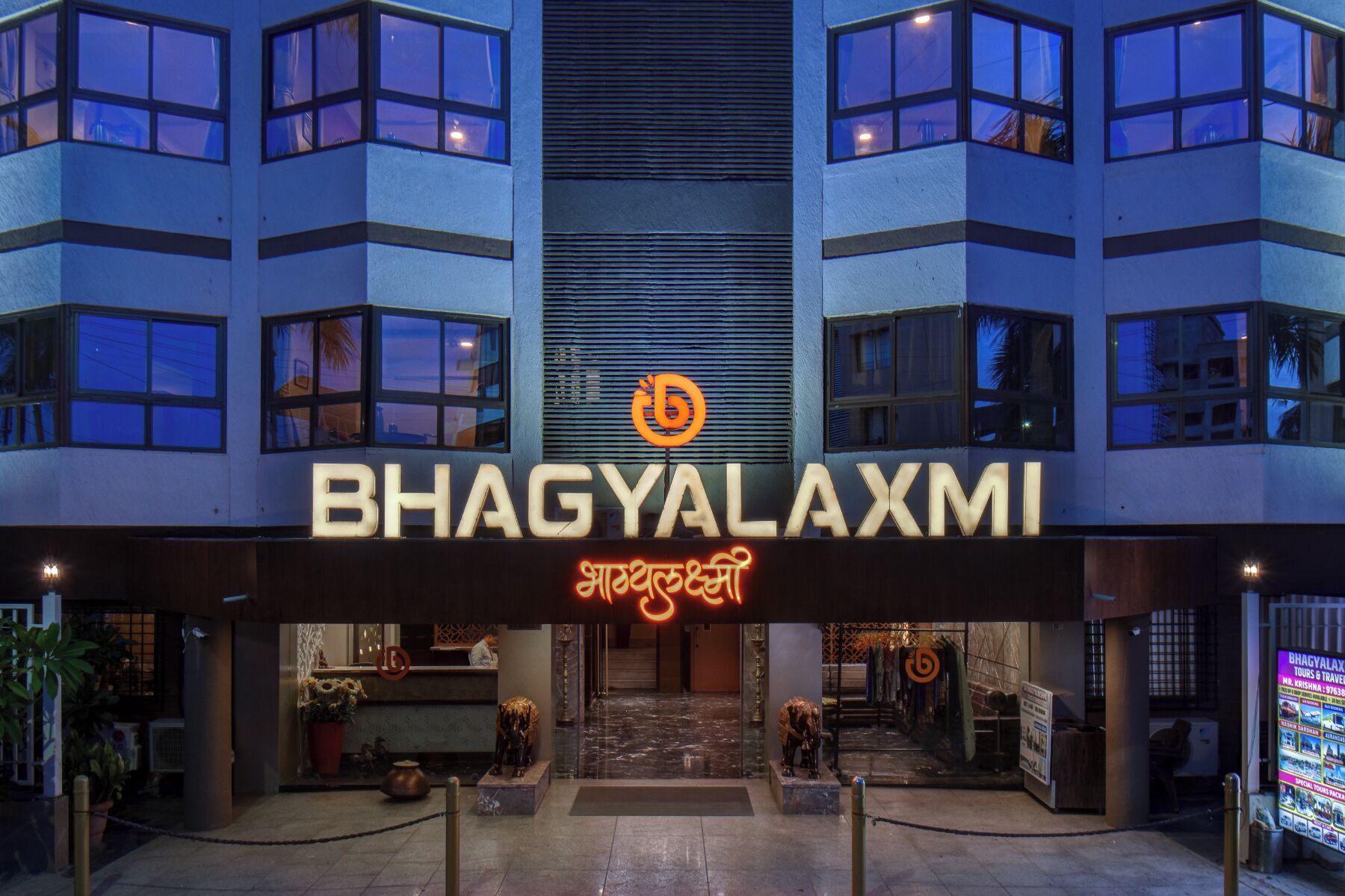 The entrance of a hotel named BHAGYALAXMI with a modern architectural design, featuring a prominent sign with the hotel's name and logo.