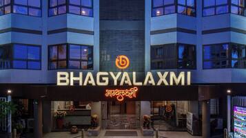 The entrance of a hotel named BHAGYALAXMI with a modern architectural design, featuring a prominent sign with the hotel's name and logo.