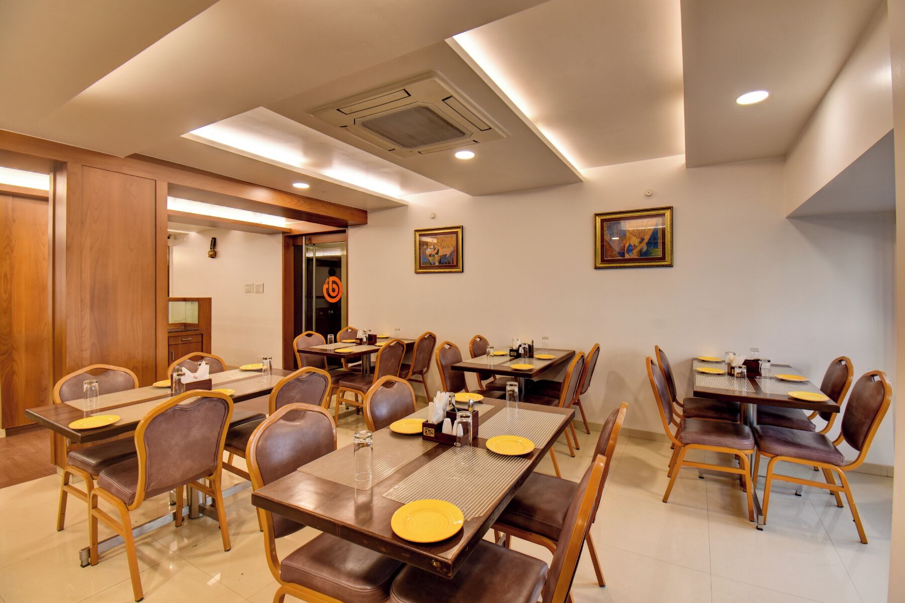 A hotel dining area with multiple tables and chairs, equipped with place settings and condiments.