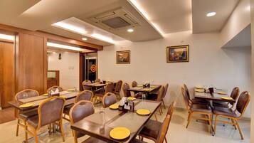 A hotel dining area with multiple tables and chairs, equipped with place settings and condiments.