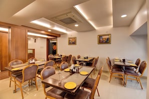 Comedor de hotel con varias mesas y sillas, mesas dispuestas con vajilla y condimentos.