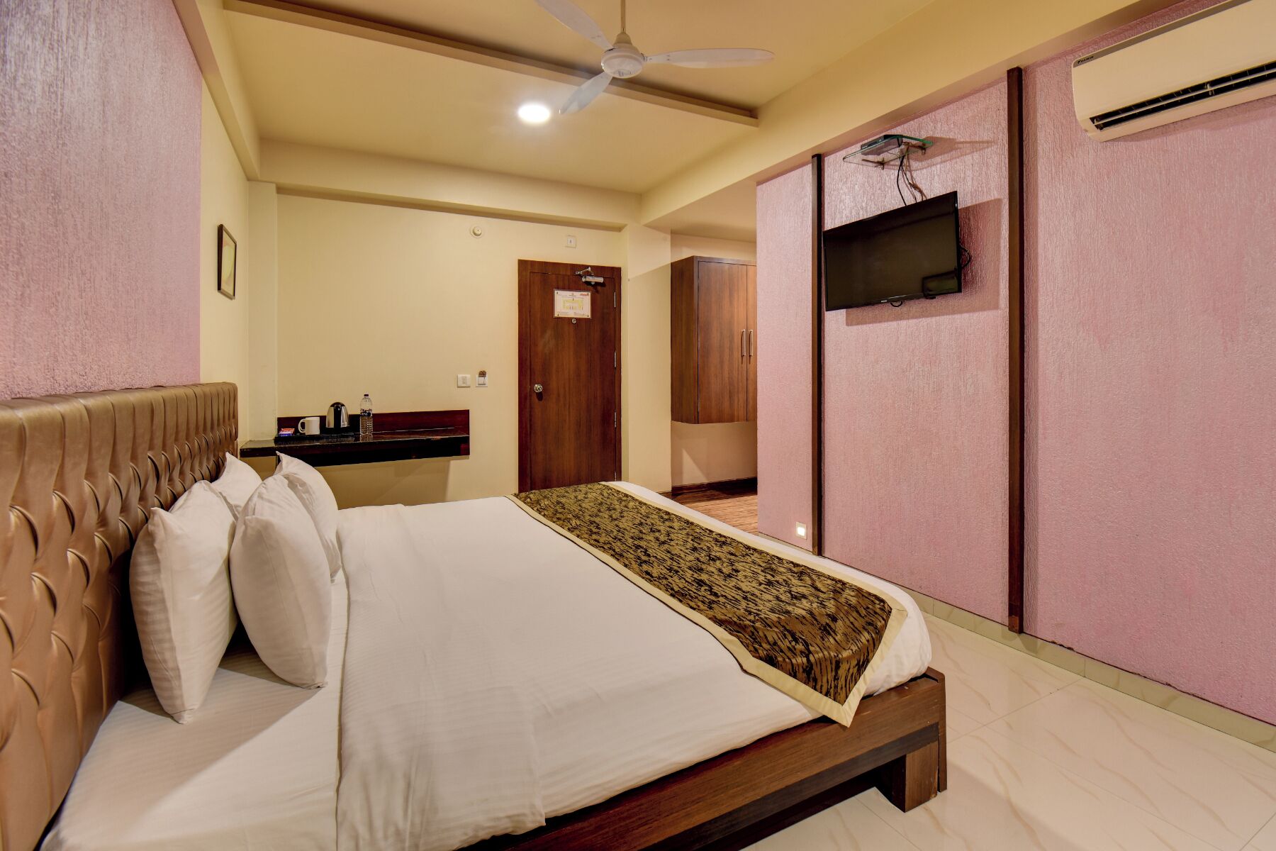 A hotel room with a bed, a ceiling fan, a television, and an air conditioning unit.