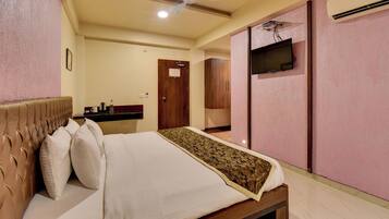 A hotel room with a bed, a ceiling fan, a television, and an air conditioning unit.
