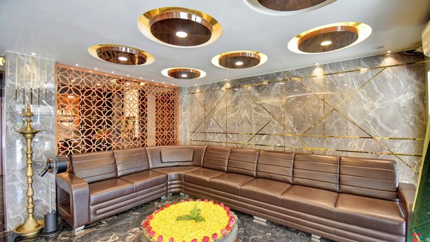 Un interior moderno con un sofá de cuero marrón curvo, una pared decorativa con motivos geométricos y una mesa central con un arreglo floral amarillo.
