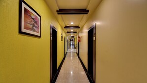 Pasillo de hotel con puertas a ambos lados, un extintor de incendios montado en la pared y un cuadro en la pared izquierda.