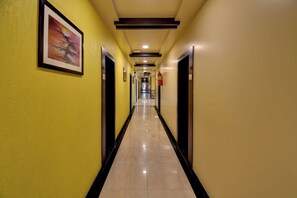 A hotel corridor with doors on both sides, a fire extinguisher mounted on the wall, and a framed picture on the left wall. - Hotel Bhagyalaxmi (Shirdi)
