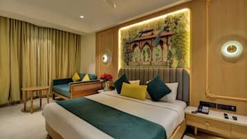 A hotel room with a large bed, a seating area with a sofa and armchair, a desk with a telephone, and a decorative wall mural.