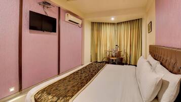 A hotel room with a bed, a small table with chairs, an air conditioning unit, and a television mounted on the wall.