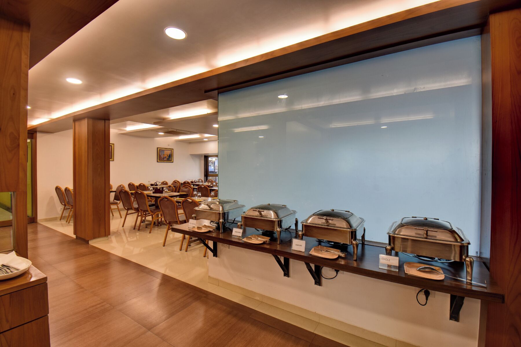 A buffet setup with multiple serving stations, each with a covered food container and labeled with a dish name.