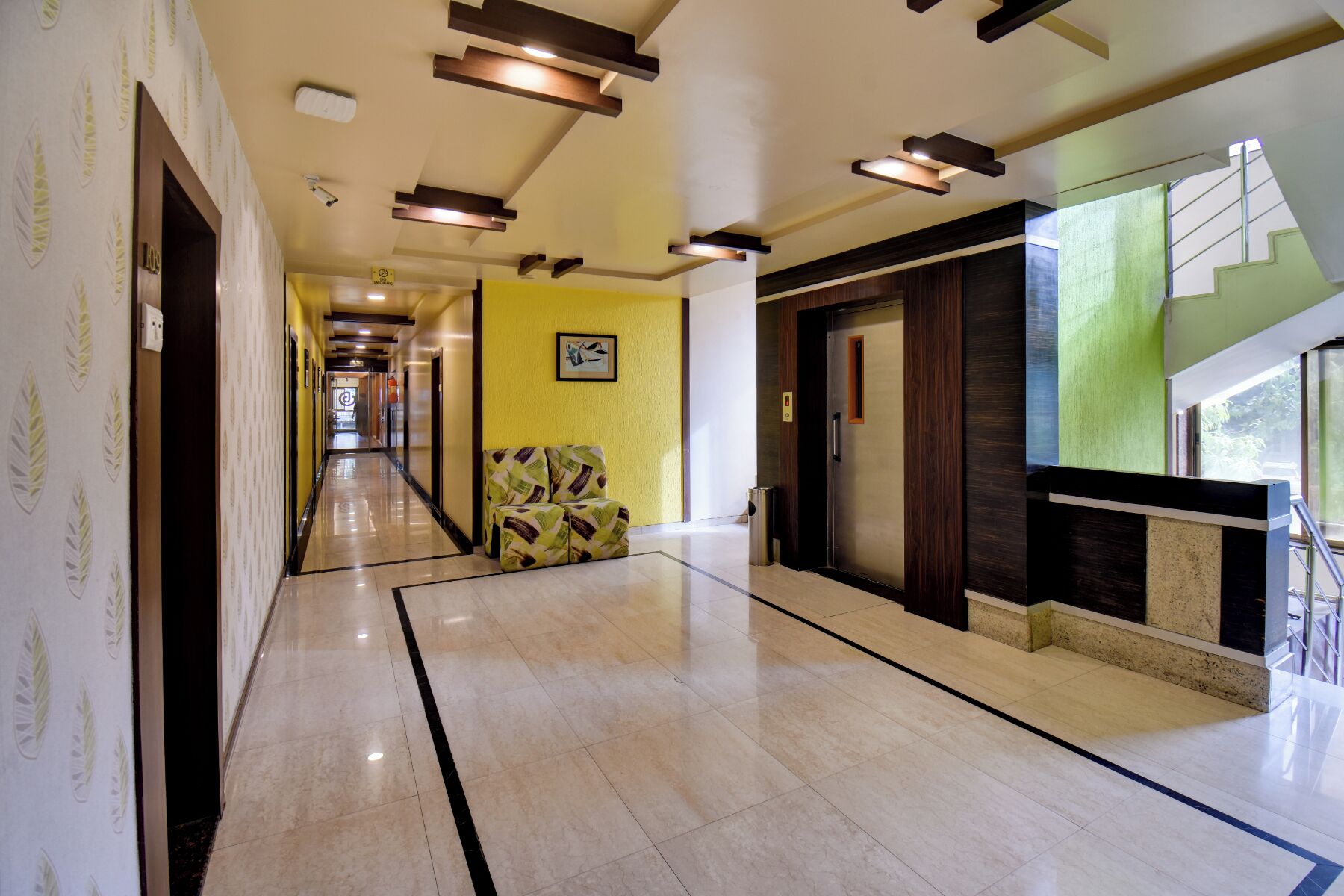 A hotel corridor with a marble floor, a sofa, a staircase, and a door with a security camera.