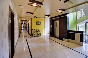 A hotel corridor with a marble floor, a sofa, a staircase, and a door with a security camera. - Hotel Bhagyalaxmi (Shirdi)