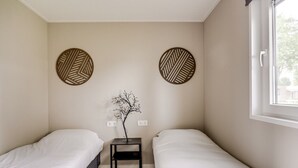 A small, clean room with two single beds, a nightstand with a decorative branch, and two wall-mounted circular decor pieces.