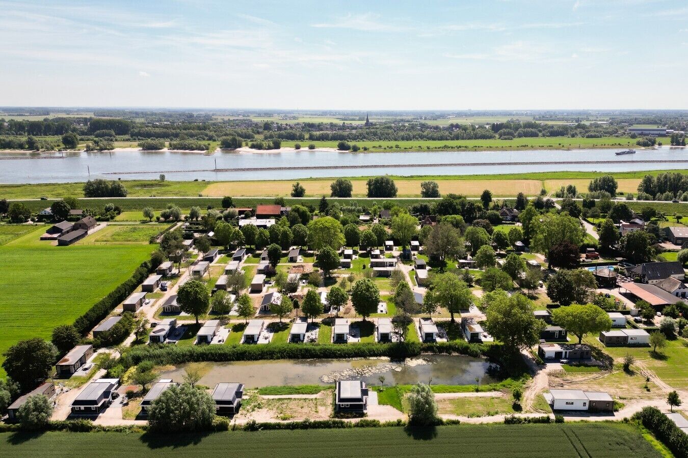 Un terrain de camping avec des camping-cars et des maisons mobiles disposés en rangées, un petit lac et un pont situé au loin.