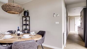 A dining area with a round wooden table, grey upholstered chairs, a woven pendant light, a black leather chair, and a black leather sofa.