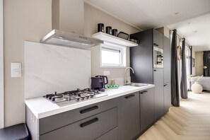 A modern kitchen with a gas stove, a coffee machine, and a sink. - Cube XL 77 | 6 persoons chalet in Zennewijnen (Zennewijnen)