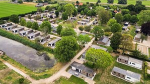 Un barrio residencial con varias casas de una sola planta dispuestas en filas, un río en primer plano y una gran masa de agua al fondo.