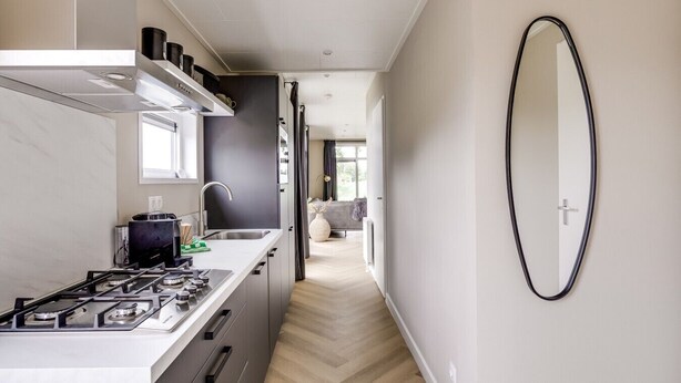 Un pasillo estrecho con una cocina a un lado y una sala de estar al otro, con un diseño moderno y decoración minimalista.