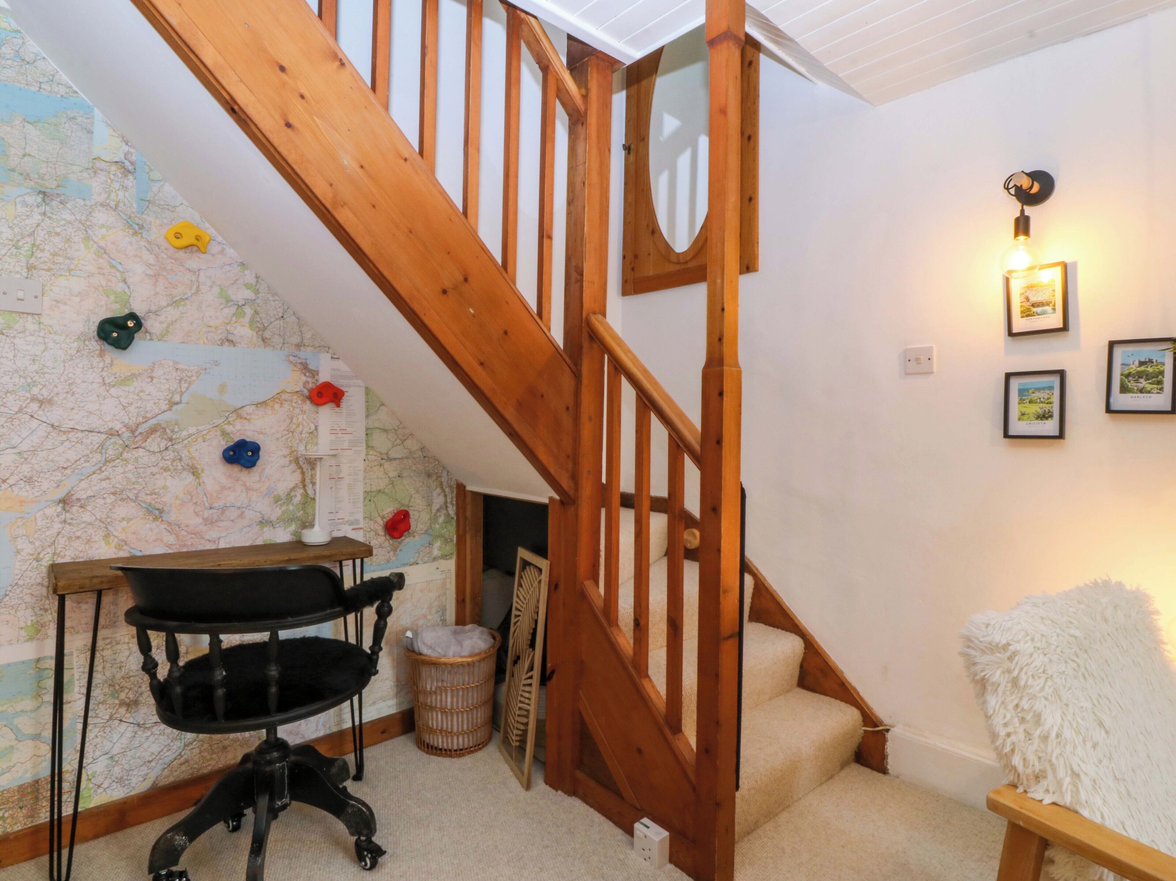 A wooden staircase, a map on the wall, a desk with a chair, and a fluffy white chair.